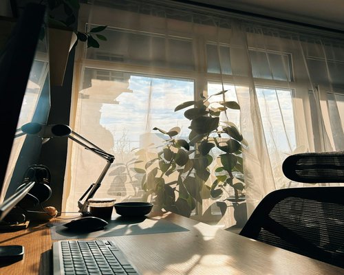 A desk setup near a window with sheer curtains diffusing sunlight