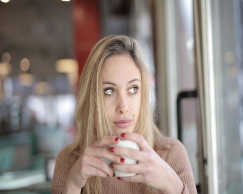 A young woman looking out the window while holding a coffee mug